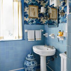 a bathroom with blue and white wallpaper has a sink, toilet, and mirror