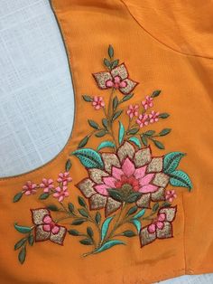 an orange top with pink flowers and green leaves embroidered on the front, sitting on a white surface