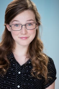 a young woman with glasses is posing for a photo in front of a blue background