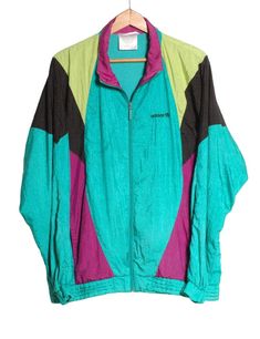 Vintage 1980's Adidas shell suit jacket. Retro design in a green, purple, yellow and black colour. Adidas trefoil embroidered on chest. Original front zip and twin waist pockets. Elasticated waist and cuffs. Made in Malaysia from a nylon fabric and fully inside lined.  Condition: Good vintage condition. Both cuffs have been repaired at some point. Chest: 44in Length: 28in Inside sleeve: 22in More vintage clothing on our website www.brickvintage.com Retro Green Windbreaker For Spring, 90s Green Windbreaker For Spring, Vintage Green Windbreaker For Fall, Vintage Green Windbreaker For Streetwear, Vintage Green Windbreaker For Winter, Retro Green Long Sleeve Windbreaker, Retro Green Windbreaker, Green 90s Style Long Sleeve Windbreaker, 90s Green Long Sleeve Windbreaker