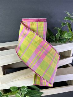 a pink and green plaid ribbon is hanging from a wooden rack with plants in the background