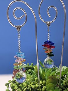 the earrings are made from glass beads and silver wire with spiral designs on them, sitting next to green plants