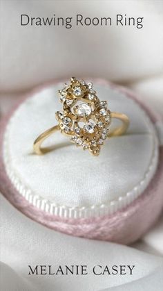 a gold ring sitting on top of a white cloth covered box with the words drawing room ring