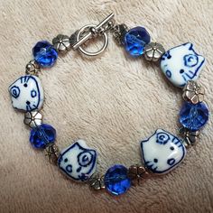 Hand Crafted Blue And White Silvertone Kitty Bracelet Cute Cobalt Blue And White Ceramic Kitty Beads With Flowers On Their Foreheads Alternate With Faceted Blue Glass Beads And Silvertone Flower Spacer Beads. Toggle Clasp Approximately 7 3/8 Inches Adorable Bracelet For Kitty Lovers! Designed And Handcrafted By Aj_nelly! Ladybug Redesign, Clay Charm Bracelet, Bracelet Supplies, Ceramic Beads Bracelet, Clay Keychain, Bracelet Cute, Bracelet Inspo, Fotos Aesthetic, Glass Bead Bracelet