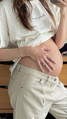 a pregnant woman sitting on a bench with her cell phone to her ear and looking at her stomach