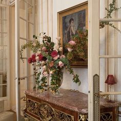 a vase with flowers sitting on top of a table in front of a painting and window