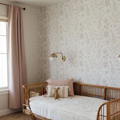 a baby's crib in front of a window with pink curtains and floral wallpaper