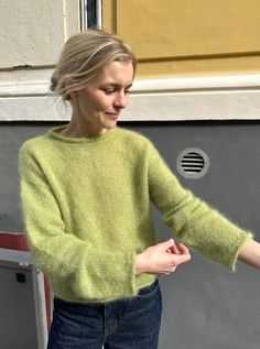 a woman wearing a green sweater and jeans is holding her hand out to the side