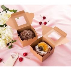 two boxes with pastries in them sitting on a pink tablecloth next to flowers