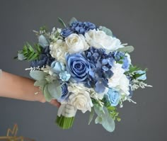 a bouquet of blue and white flowers in someone's hand on a gray background