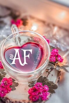 a heart shaped glass with the letter m on it and some pink flowers around it