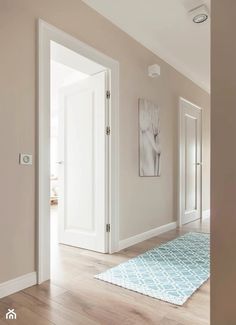 an empty hallway with white doors and wood flooring is seen in this image from across the room