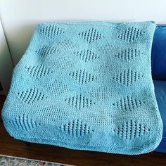 a blue crocheted blanket sitting on top of a blue couch next to a white wall