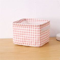 a pink and white checkered basket sitting on top of a wooden table next to a wall