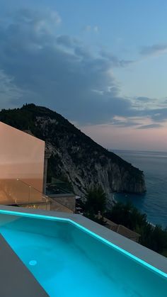 an outdoor swimming pool next to the ocean at night with lights on and water reflecting off it's surface