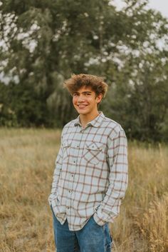 a young man standing in the middle of a field smiling and looking at the camera