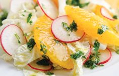 a salad with oranges, radishes and cucumbers on a white plate