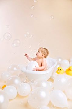 a baby in a bathtub surrounded by balloons and rubber ducks