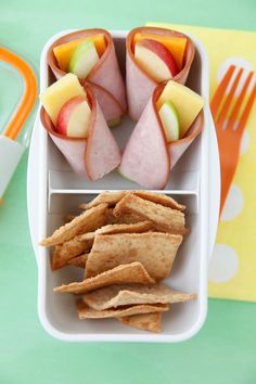 an assortment of fruit and crackers in a container on a table with utensils