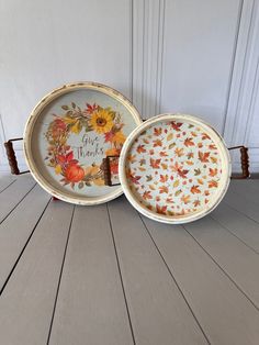 two plates with autumn designs on them sitting on a wooden floor next to each other