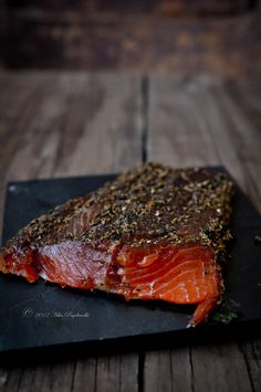 a piece of raw salmon on a black plate with seasoning sprinkles