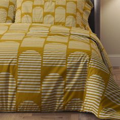 a bed with yellow and white comforter on top of wooden floor next to lamp