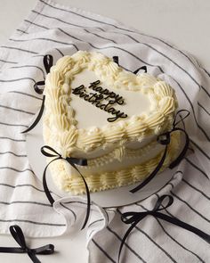 a heart shaped cake on a white plate with black ribbon around it and the words happy birthday written in frosting