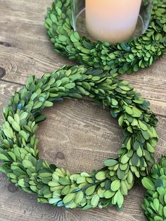 a candle is sitting next to a wreath on a wooden table with green leaves around it