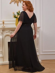 a woman standing in front of a fire place wearing a black dress with sheer sleeves