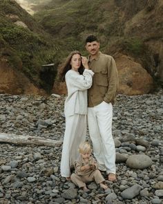 a man and woman standing next to a child on a rocky beach