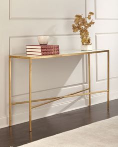 a gold console table with two books on top and a vase filled with flowers next to it