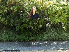 a woman is standing in between two bushes