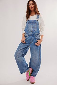 a woman in overalls and pink shoes posing for the camera with her hands on her hips