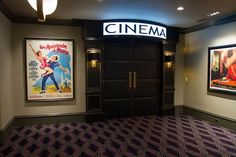 the entrance to a movie theater with posters on the wall and carpeted flooring