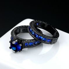 two black gold rings with blue sapphire stones on top of each other, sitting on a white surface