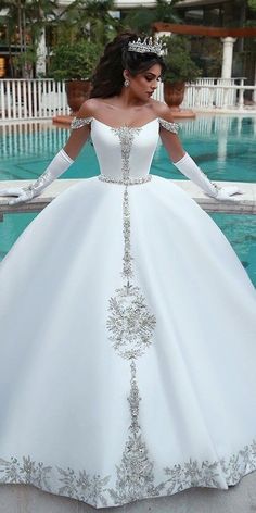 a woman in a white wedding dress standing next to a pool wearing a tiara