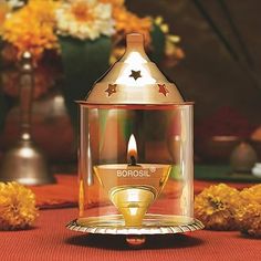 a candle that is sitting in a glass container on a table with flowers behind it