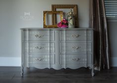 a white dresser sitting next to a window with a gold framed picture on top of it