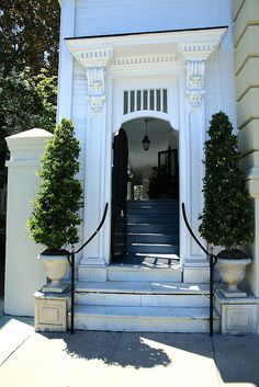 an entrance to a white house with steps and potted plants on the front porch