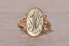 The Rouge: Vintage Signet Ring in Yellow Gold. This elegant ring features an elongated oval top oriented North to South, adorned with a hand-engraved monogram at the center, which can be customized with your initials for an additional $250 upon request. Flanking the center, patterned double split shanks complete the look, adding depth and dimension to the design. Crafted in 14 karat yellow gold, the ring exudes warmth and sophistication. Currently sized at 3, it can be adjusted to fit any finger Antique Oval Signet Ring With Polished Finish, Luxury Oval Cabochon Signet Ring For Anniversary, Classic Oval Engraved Ring For Formal Occasions, Elegant Signet Ring With Oval Cabochon And Polished Finish, Timeless Oval Engraved Ring With Polished Finish, Elegant Hallmarked Signet Ring For Formal Occasions, Elegant 14k Gold Engraved Initials Ring, Elegant Formal Hallmarked Signet Ring, Victorian Oval Signet Ring With Polished Finish