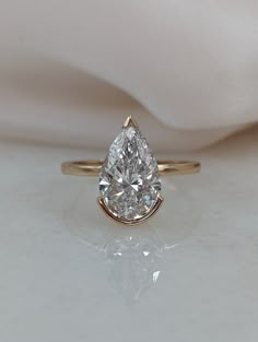 a pear shaped diamond ring sitting on top of a white cloth