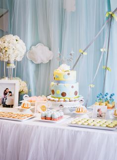 a table topped with lots of cakes and cupcakes next to a wall covered in clouds