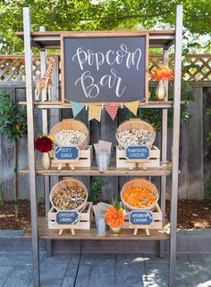 an outdoor popcorn bar is set up on a wooden stand with chalkboard sign above it