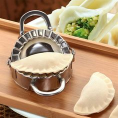 some dumplings are sitting on a wooden tray next to a silver teapot and saucer