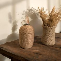 two vases with dried plants in them sitting on a wooden table next to a wall