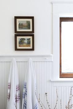 two white towels hanging on the wall next to a window with framed pictures above it