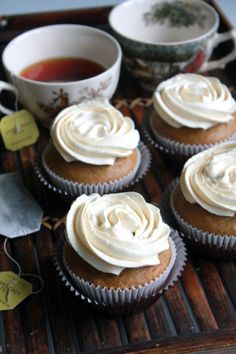 cupcakes with white frosting sitting on a wooden tray next to tea cups