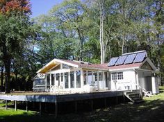 a small house with solar panels on the roof and windows in front of it, surrounded by trees