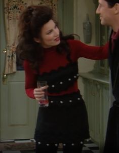 a woman in a red shirt and black skirt standing next to a man in a kitchen