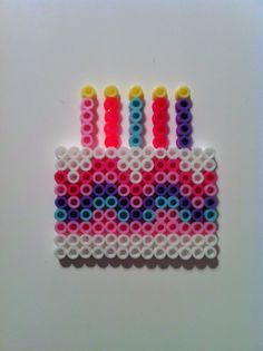 a piece of art made out of beads with candles on it's side, sitting on a white surface